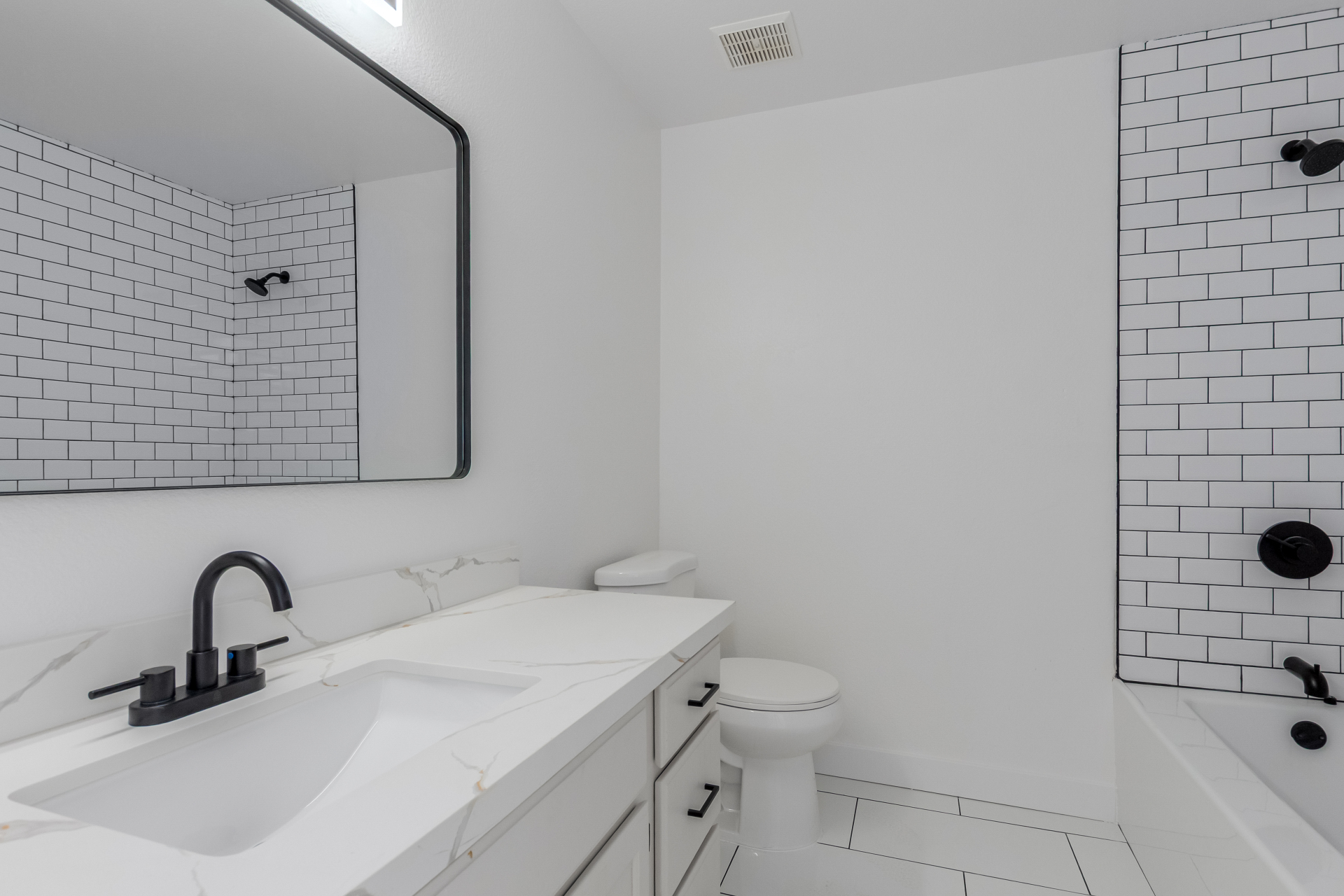 Full bathroom remodel with subway tile tub surround, marble-look vanity, and matte black hardware