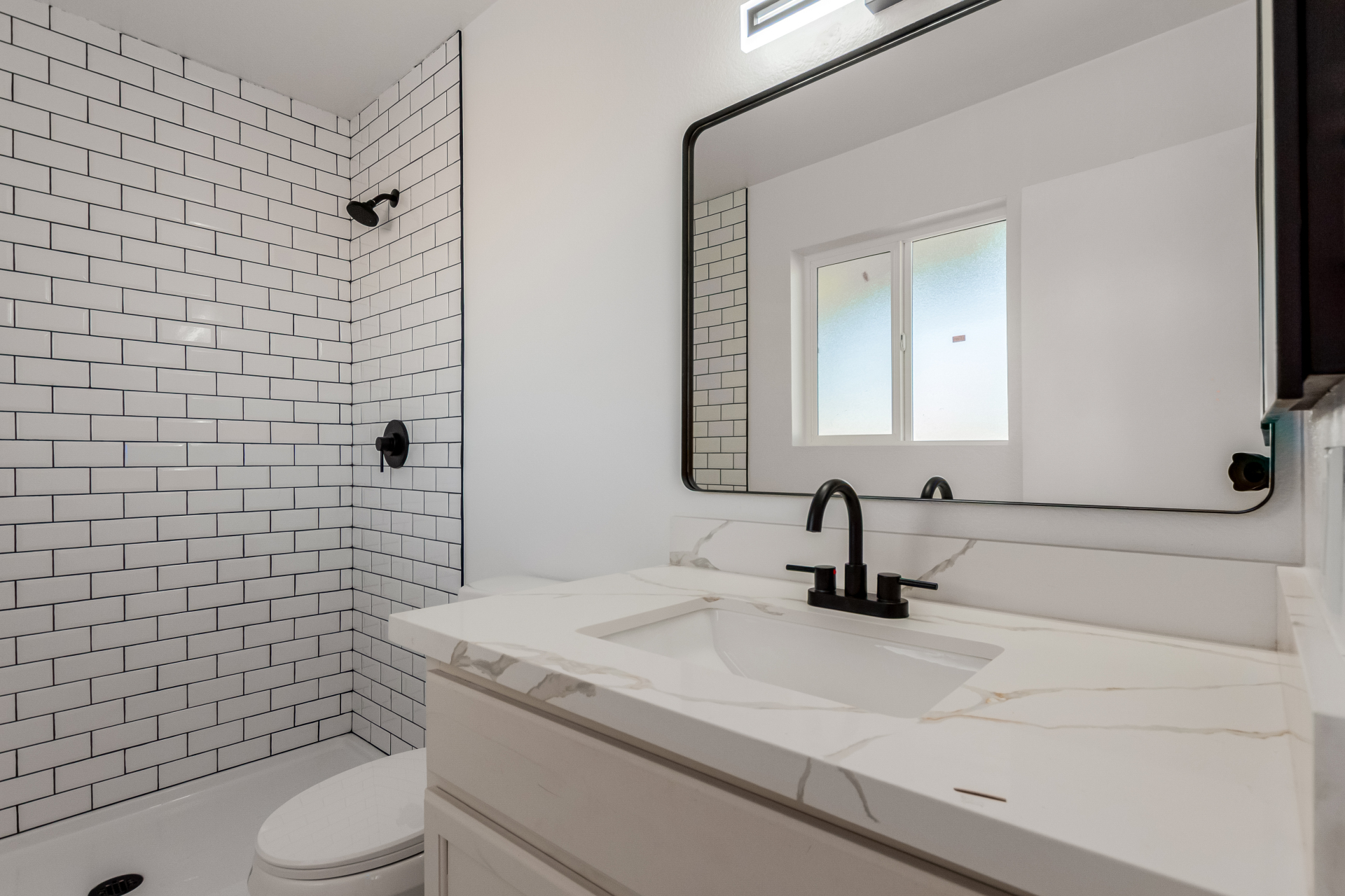 Modern bathroom remodel with white subway tile shower, black fixtures, and quartz vanity